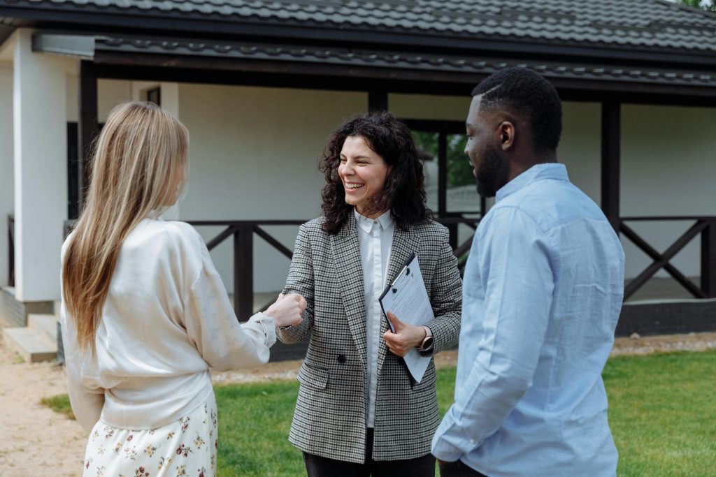 A female realtor shaking hands with the wife of a couple outside a home - Visit afinestpm.com. 